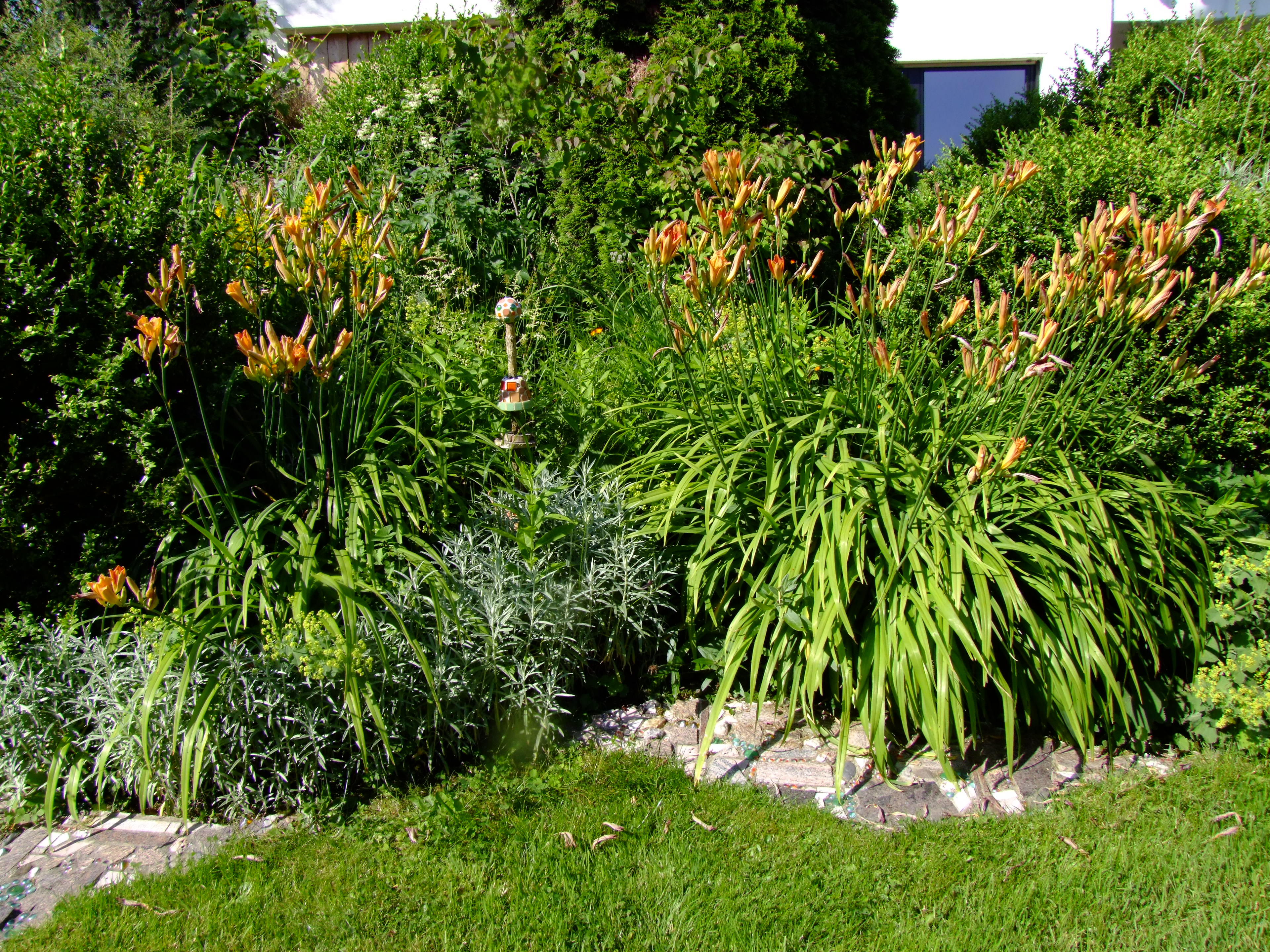 Die Stauden überwuchern im Sommer die Deko und Beeteinfassungen aus Mosaiken.