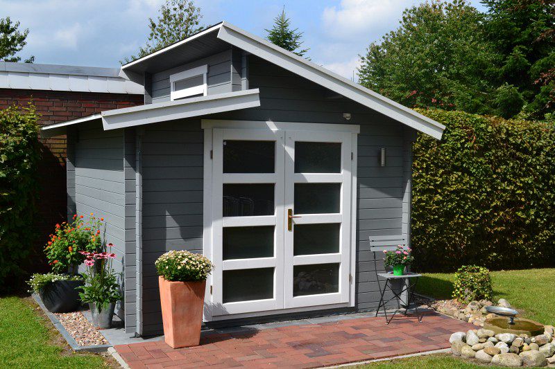 Aktiva-40 ist nicht ohne Grund eines unserer beliebtesten Gartenhaus-Modelle: Mit grau-weißem Anstrich passt es auch perfekt zu roten Terrassen-Fliesen.