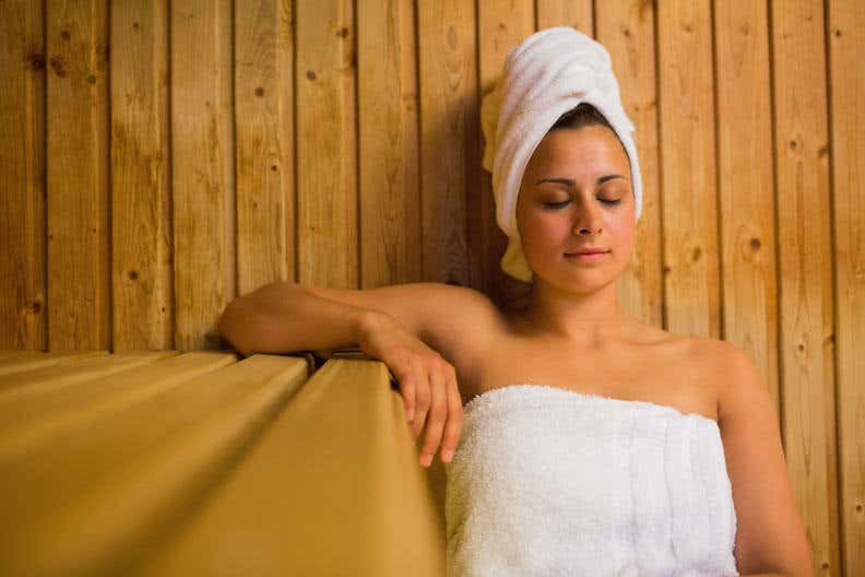 Frau sitzt mit Handtuch in Sauna