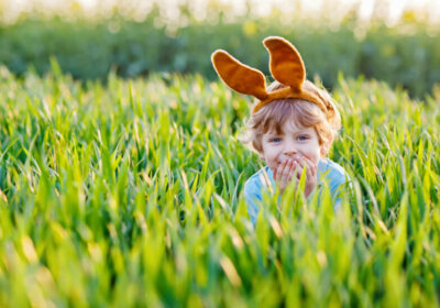 Kreative Verstecke für das Osterfest im Garten Kind mit Hasenohren im Gras